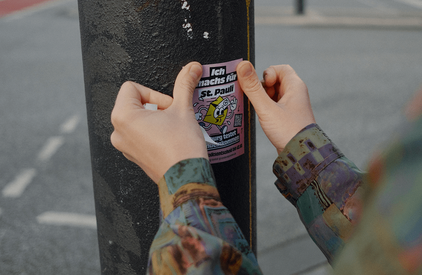 Hände kleben einen Kampagnen-Sticker auf einen Laternenpfahl